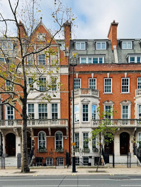 A row of elegant white or cream-colored terrace houses with ornate architectural details, including protruding bay windows and decorative moldings. The ground floors feature small, covered porches sup